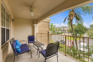 A balcony with a table and two chairs, a ceiling fan, and a view of a residential area with palm trees and a road. - Work, Play and Stay, 3br, Prime Orlando Location (Orlando)