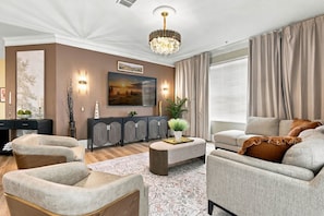 A modern living room with a chandelier, sofas, a coffee table, and a large painting on the wall. - Upscale Vista Cay 3BR With Resort Pool View (Orlando)