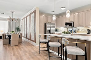 A modern kitchen with a central island, bar stools, and pendant lighting. - Upscale Vista Cay 3BR With Resort Pool View (Orlando)
