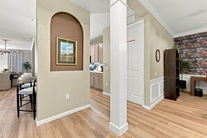 A spacious living area with a dining table, chairs, a kitchen in the background, and a decorative wall with a clock. - Upscale Vista Cay 3BR With Resort Pool View (Orlando)