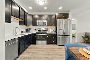 A modern kitchen with dark cabinets, stainless steel appliances, and a wooden dining table. - Work and Play, Spacious 3BR at Vista Cay (Orlando)