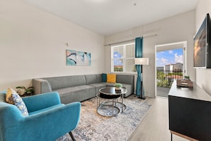 A modern living room with a grey sofa, blue armchairs, a round coffee table, and a TV on a stand. - Work and Play, Spacious 3BR at Vista Cay (Orlando)