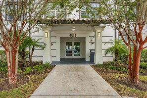 A building entrance with a number '4013' above the doors, surrounded by trees and a pathway leading to the entrance. - Work and Play, Spacious 3BR at Vista Cay (Orlando)