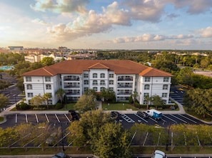 A multi-story residential building with a red-tiled roof, parking lot, and surrounding greenery. - Spacious 3br, Near Parks and Convention Center (Orlando)