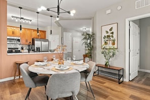 A modern kitchen with stainless steel appliances, a dining area with a round table and grey upholstered chairs, and a living space with a large potted plant. - Vista Cay 3br, Comfort & Prime Location, Sleeps 7 (Orlando)