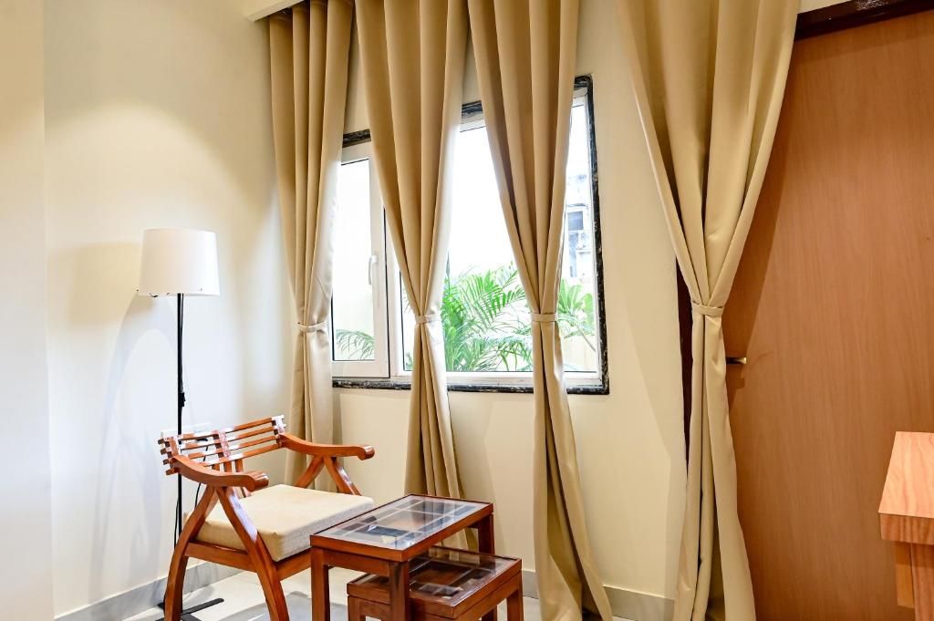Une pièce avec une chaise en bois, une petite table, un lampadaire et une fenêtre avec des rideaux.