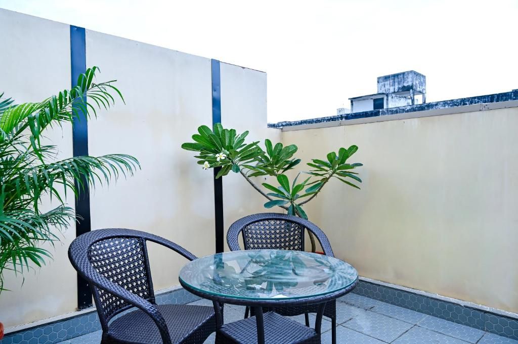 Une table à plateau en verre, accompagnée de deux chaises, entourée de plantes en pot, le tout placé devant un mur orné d’une bande bleue et sur un sol carrelé.