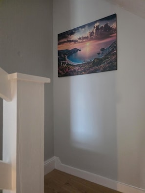 A room with a painting of a sunset over a body of water on the wall.