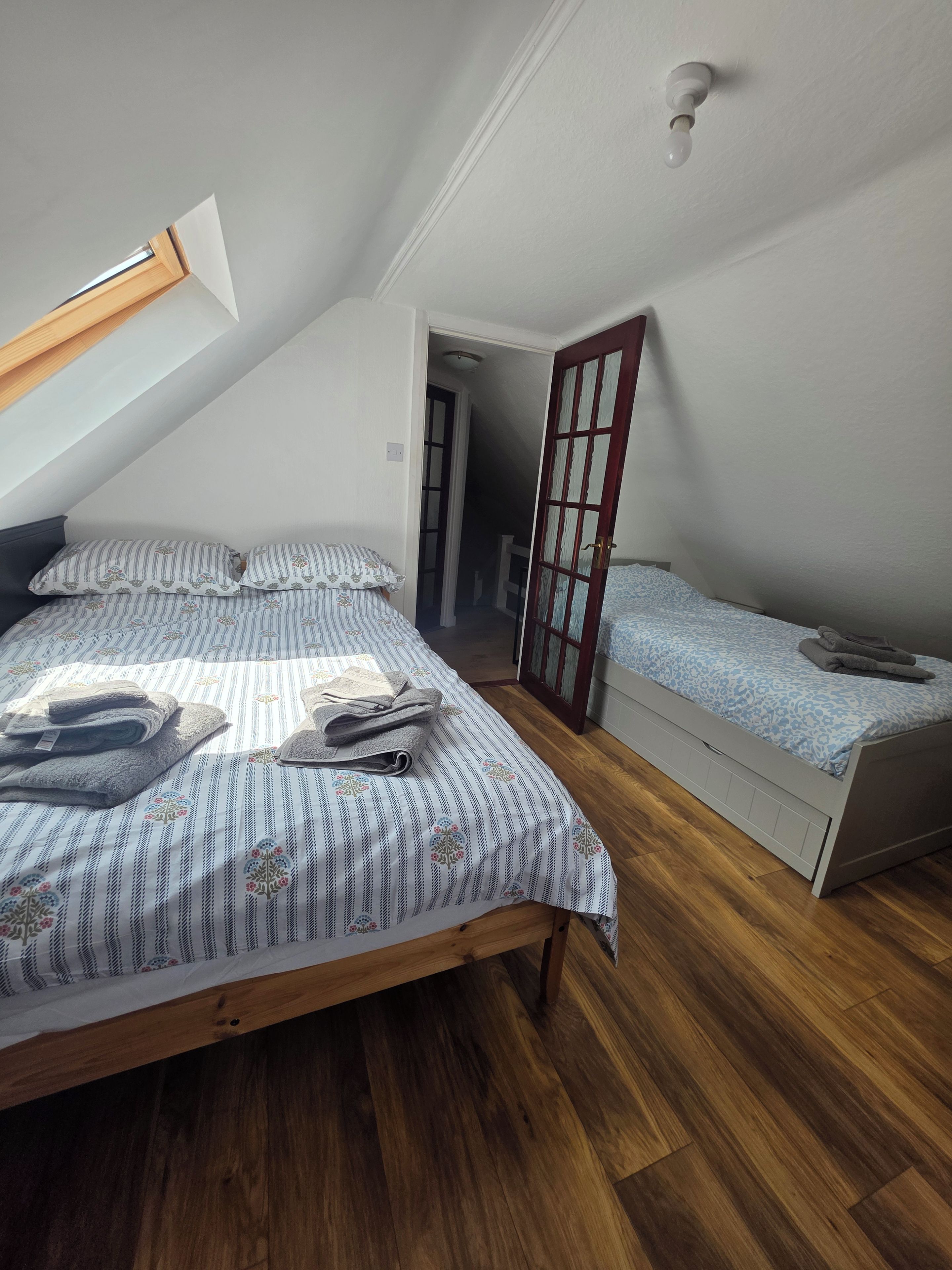 A bedroom with a sloped ceiling, a bed with striped bedding, a bedside table, and a wooden floor.