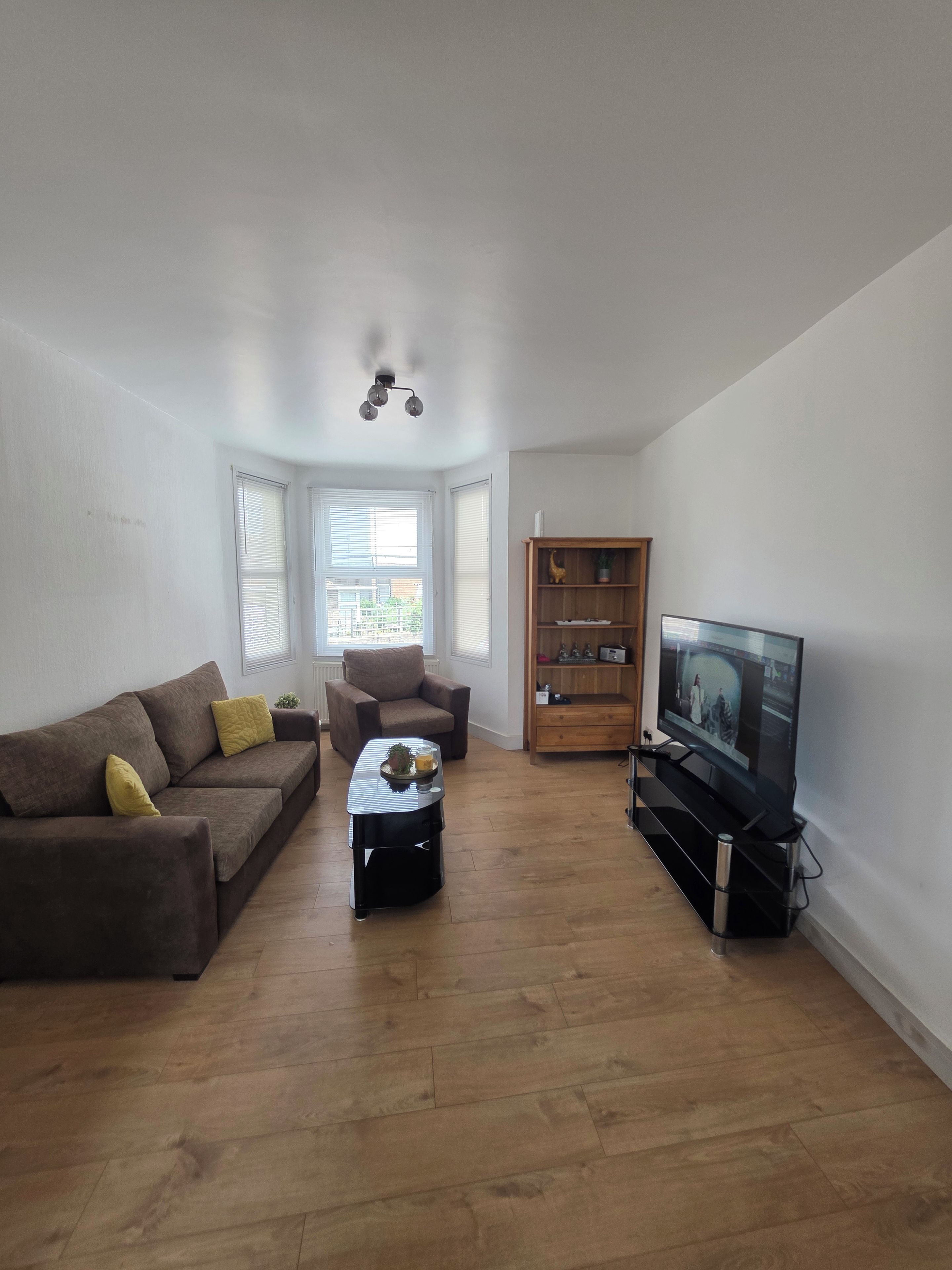 Een woonkamer met een bank, fauteuil, salontafel, televisie en een boekenplank.