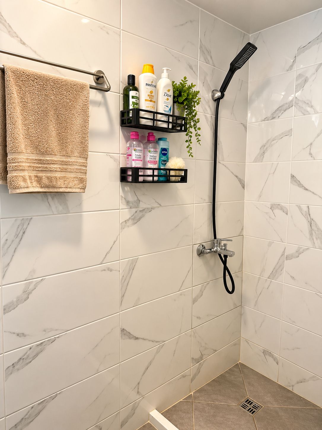 A bathroom with a shower, marble tiles, a towel rack, and a shelf with toiletries.