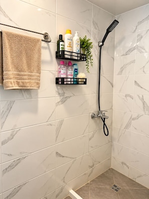 Un baño con ducha, azulejos de mármol, un perchero y un estante con artículos de aseo.
