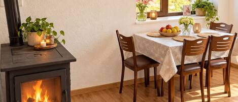 Un comedor acogedor con estufa de leña, una mesa dispuesta para cuatro personas y una ventana con vistas a la vegetación.