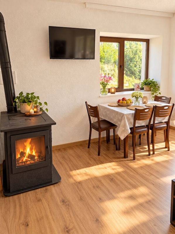 A cozy dining area with a wood-burning stove, a table set for four, and a window with a view of greenery.