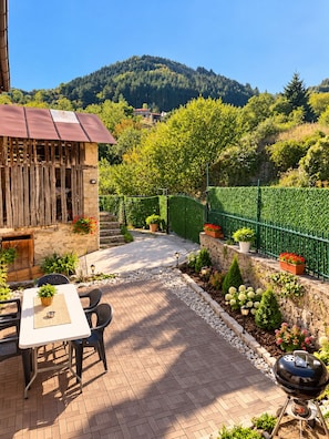 A patio area with a table and chairs, a barbecue grill, and a stone wall with potted plants.