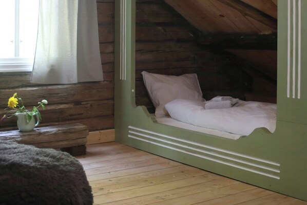A cozy attic bedroom with a wooden floor, a bed with white bedding, and a small table with a vase of flowers. - Idyll, history and nature – all in one place (Hornnes)