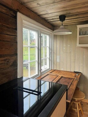 A kitchen with a black countertop, wooden cabinets, and a window with a view of greenery. - Idyll, history and nature – all in one place (Hornnes)