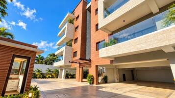 A modern multi-story building with a flat roof, large windows, and a covered outdoor area with a paved floor.