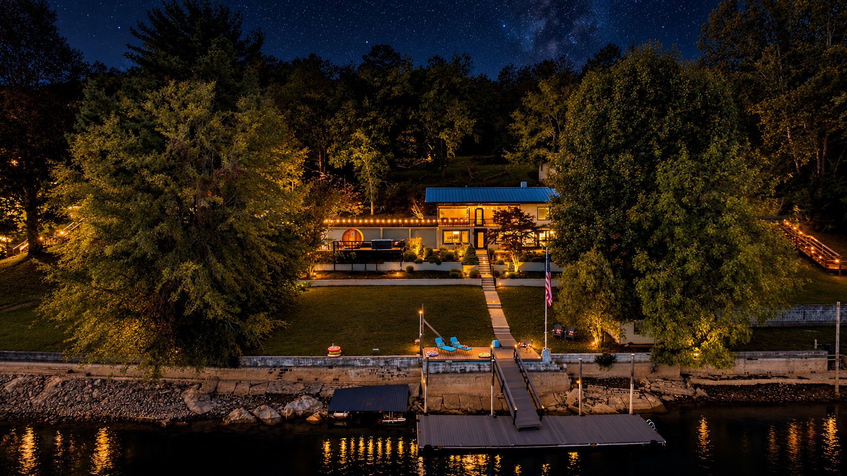 A waterfront property with a dock, a pool, and a building with outdoor lighting.