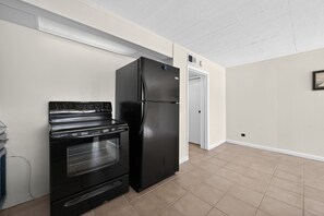 A kitchen with a black refrigerator and oven, beige tiled floor, white walls, and a door leading to another room. - Lake House on Boone Lake (Kingsport)