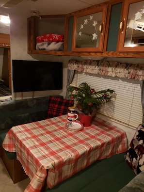 Ein Zimmer mit kariertem Tisch, einem Fernseher, einem Weihnachtsbaum und einer Vitrine mit Dekoration.