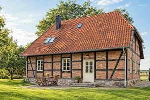 Ein traditionelles Fachwerkhäuschen mit Ziegeldach, Schornstein und einem kleinen Garten mit Tisch und Stühlen.