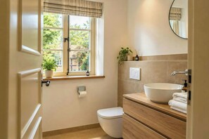 A bathroom with a toilet, a sink, a window with a view of greenery, and a mirror. - Apartment in the Countryside near Nature Reserve (Häuslingen)