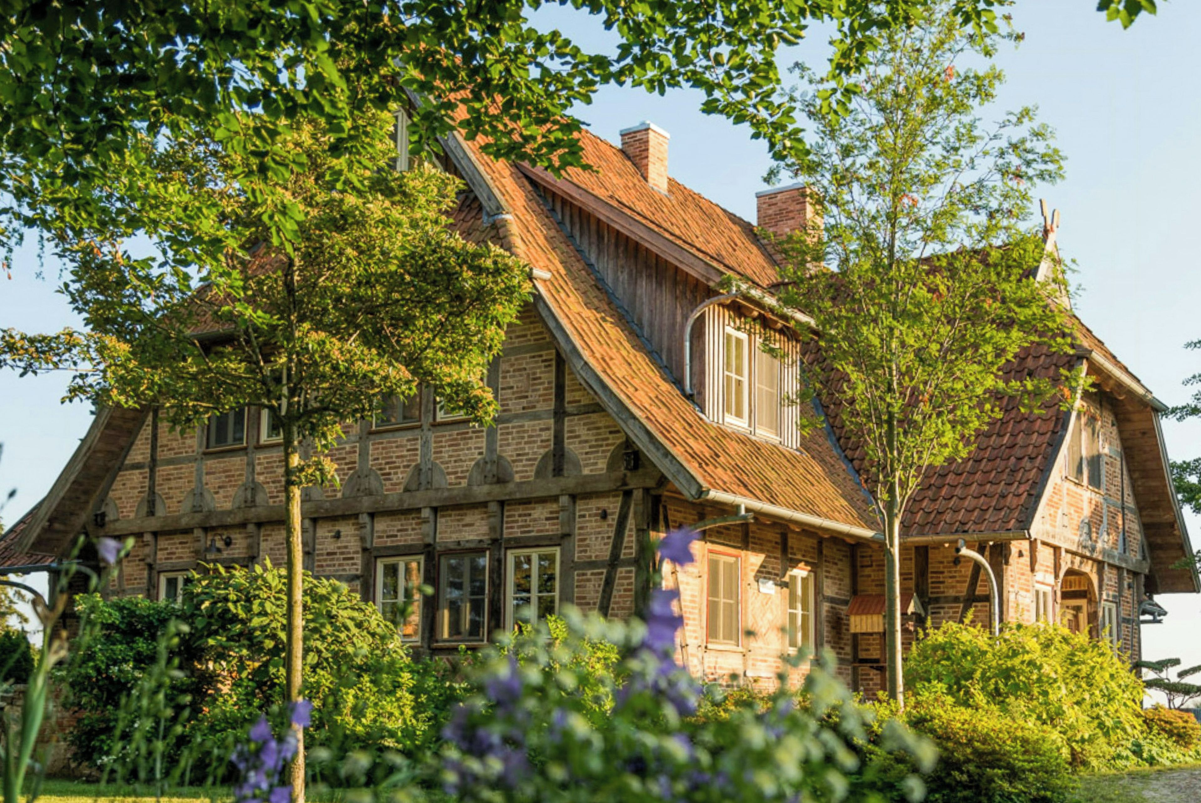 A traditional brick house with a steeply pitched roof, multiple windows, and a well-maintained garden.