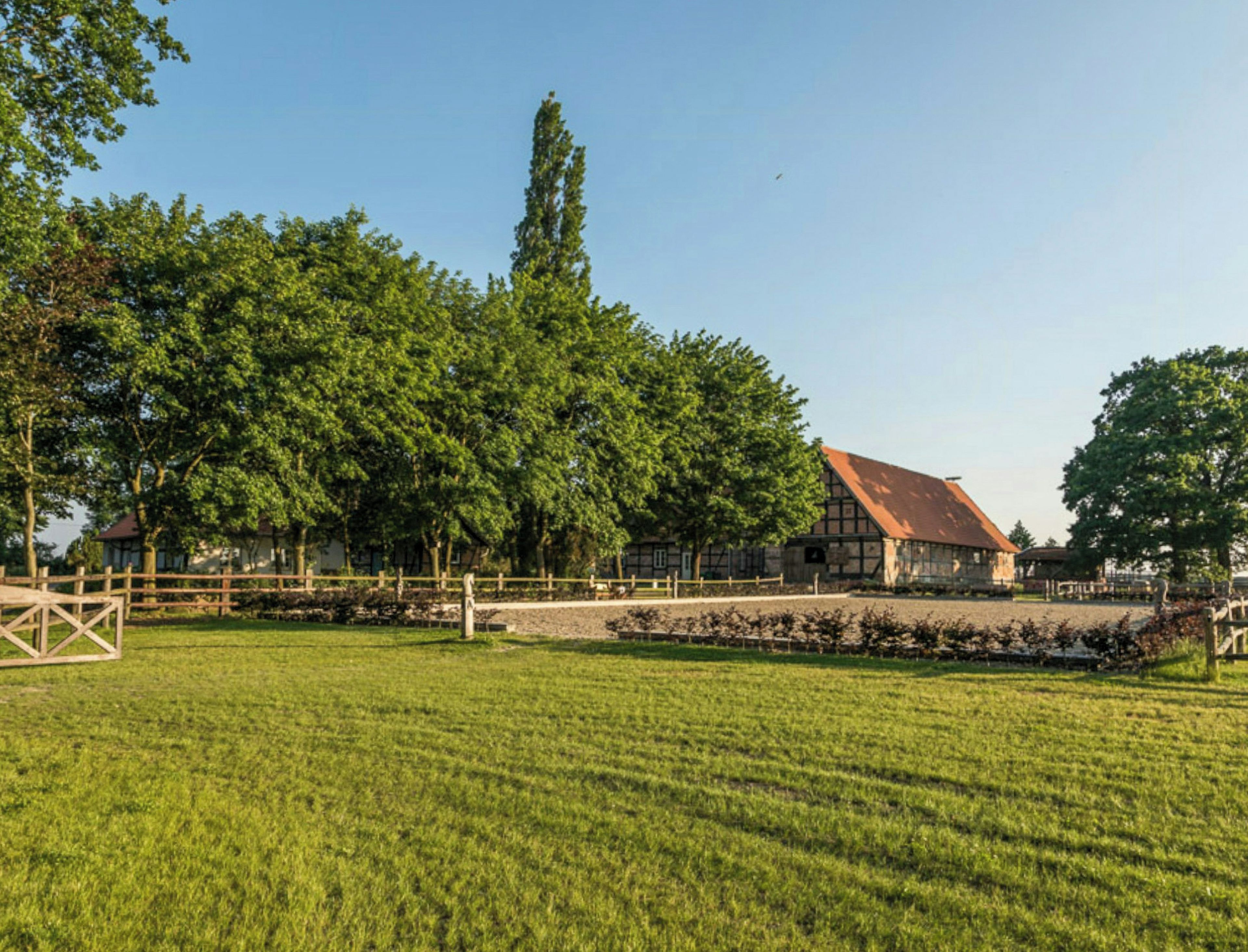 Een landelijke omgeving met een groot open veld, een traditioneel gebouw met schuin dak en een houten omheining.
