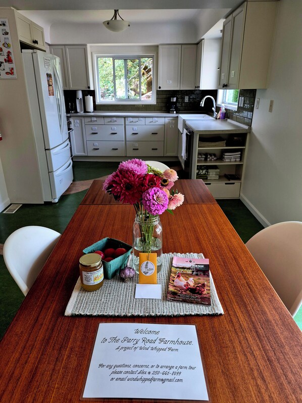 A kitchen with white cabinets, a dining table with a placemat, a vase with flowers, and a welcome sign.