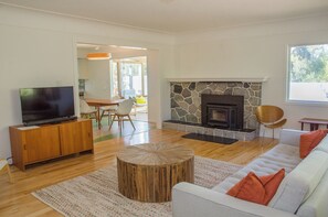 A modern living room with a stone fireplace, wooden furniture, and a television on a cabinet. - Farm stay in the heart of Metchosin, near Victoria and outdoor adventures (Victoria)