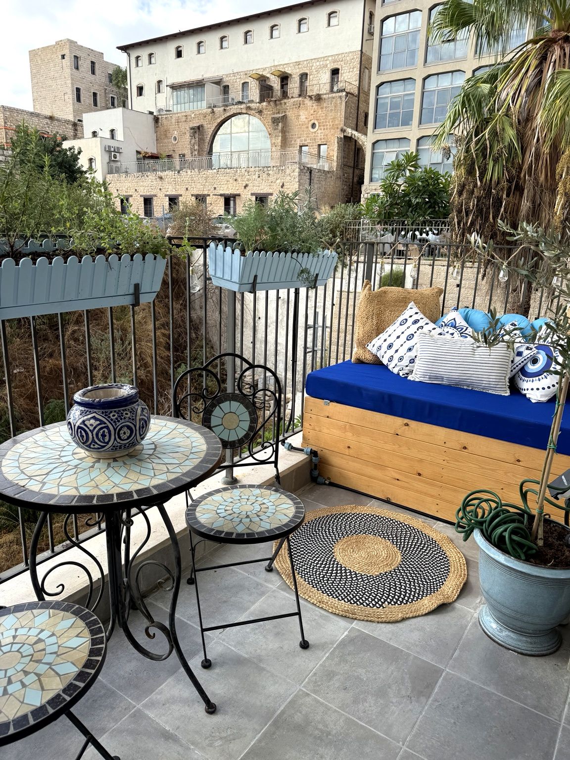 A balcony with a blue sofa, patterned cushions, a mosaic table, and a potted plant.