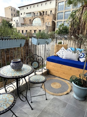 A balcony with a blue sofa, patterned cushions, a mosaic table, and a potted plant. - Little greece - Charming Haifa Downtown Apartment (Haifa)