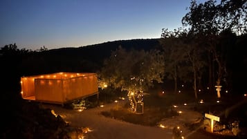 Une structure en bois, avec une pancarte indiquant « BIENVENUE » à son entrée, entourée d’un sentier illuminé par de petites lumières.