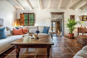 A cozy living room with a wooden coffee table, a sofa with cushions, a potted plant, and a rustic wooden door. - Rural cortijo with pool and Mediterranean views (Canillas de Aceituno)