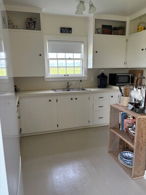 A kitchen with white cabinets, a window, a sink, a microwave, and a wooden shelf with books and kitchenware. - Two-story farmhouse on a working alfalfa farm, minutes from the wine district (Walla Walla)