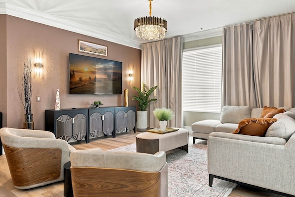 A modern living room with a sofa, armchairs, a coffee table, a TV, and a decorative plant. - Upscale Vista Cay 3BR With Resort Pool View (Orlando)