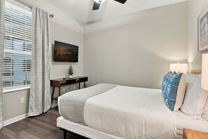 Ein Schlafzimmer mit einem Bett, einem Schreibtisch, einem Fernseher und einem Fenster mit Vorhängen.
