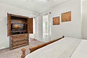 A bedroom with a bed, a wooden dresser with a TV, a door, and two wall decorations. - Work Play and Stay 3BR Prime Orlando Location (Orlando)