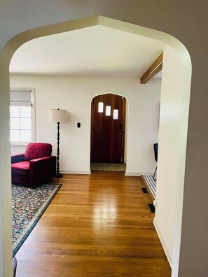 Un couloir doté d’un plancher en bois, d’une chaise rouge, d’une lampe et d’une porte avec une petite fenêtre.