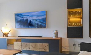 A modern hotel room with a flat-screen TV mounted on the wall, a wooden console table with a lamp, and a decorative canister. - CONTEMPORARY ALPINE APARTMENT WITH TWO BATHROOMS AND MOUNTAIN VIEWS (Zermatt)