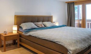 A single bed with a wooden headboard, a bedside table with a lamp, and a view of a balcony. - CONTEMPORARY ALPINE APARTMENT WITH TWO BATHROOMS AND MOUNTAIN VIEWS (Zermatt)