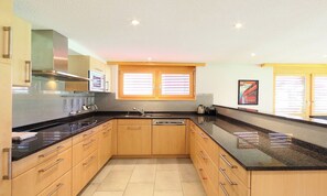 A modern kitchen with wooden cabinets, a black countertop, and a built-in oven. - CONTEMPORARY ALPINE APARTMENT WITH TWO BATHROOMS AND MOUNTAIN VIEWS (Zermatt)