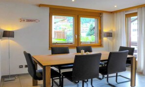 Ein Essbereich mit einem Holztisch und schwarzen Stühlen, einem Fenster mit Vorhängen sowie einer Wandleuchte.