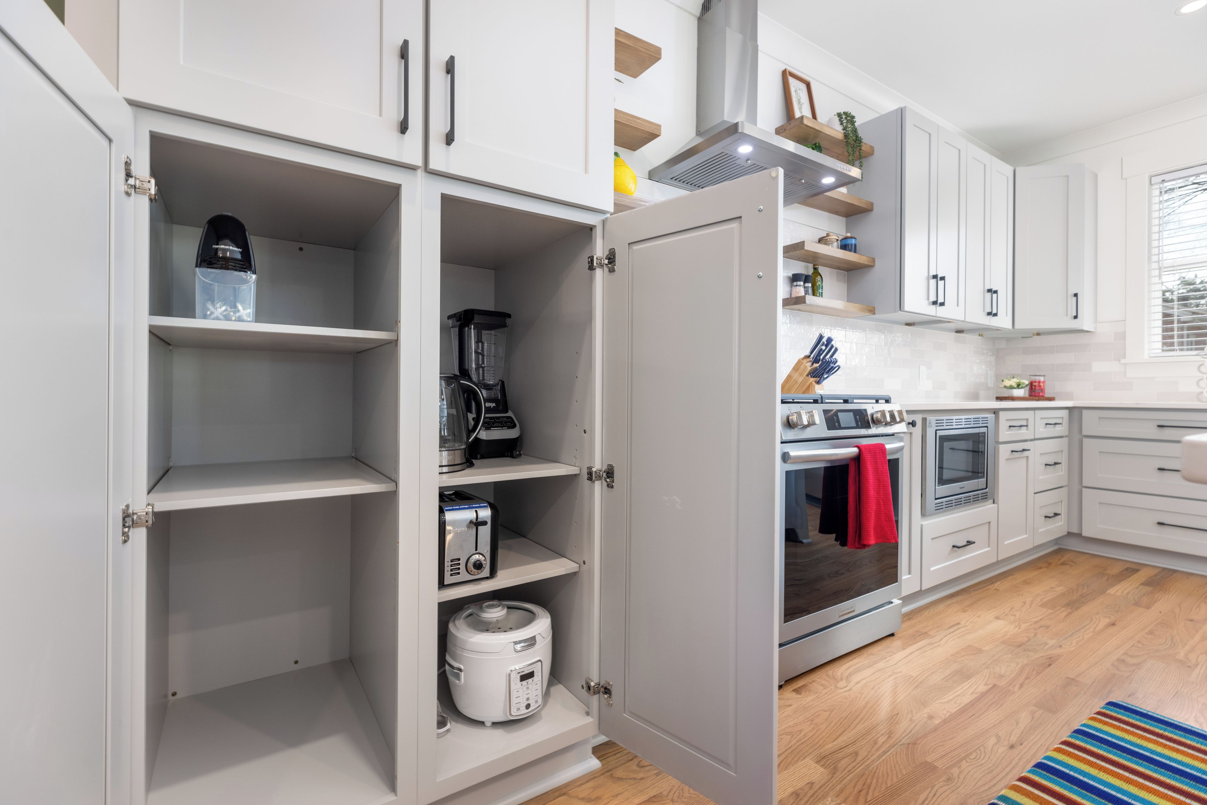 Een moderne keuken met witte kasten, een inbouwoven en diverse apparaten, waaronder een blender en een rijstkoker.