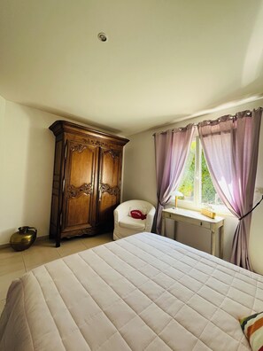 Un dormitorio con cama, armario de madera, una silla, escritorio y ventana con cortinas.