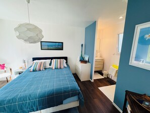 Ein Schlafzimmer mit einem Bett, einem Nachttisch, einem Fenster und einem durch eine offene Tür einsehbarer Badezimmer.