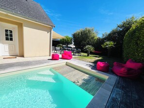 Piscina con una fuente de agua azul cristalina, rodeada por una terraza con mobiliario exterior y un jardín.