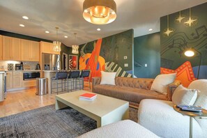 A modern living room with a sofa, coffee table, and a kitchen area with a refrigerator and microwave. - Off Broadway Nashville: Rooftop Hot Tub & Skyline Views (Nashville)