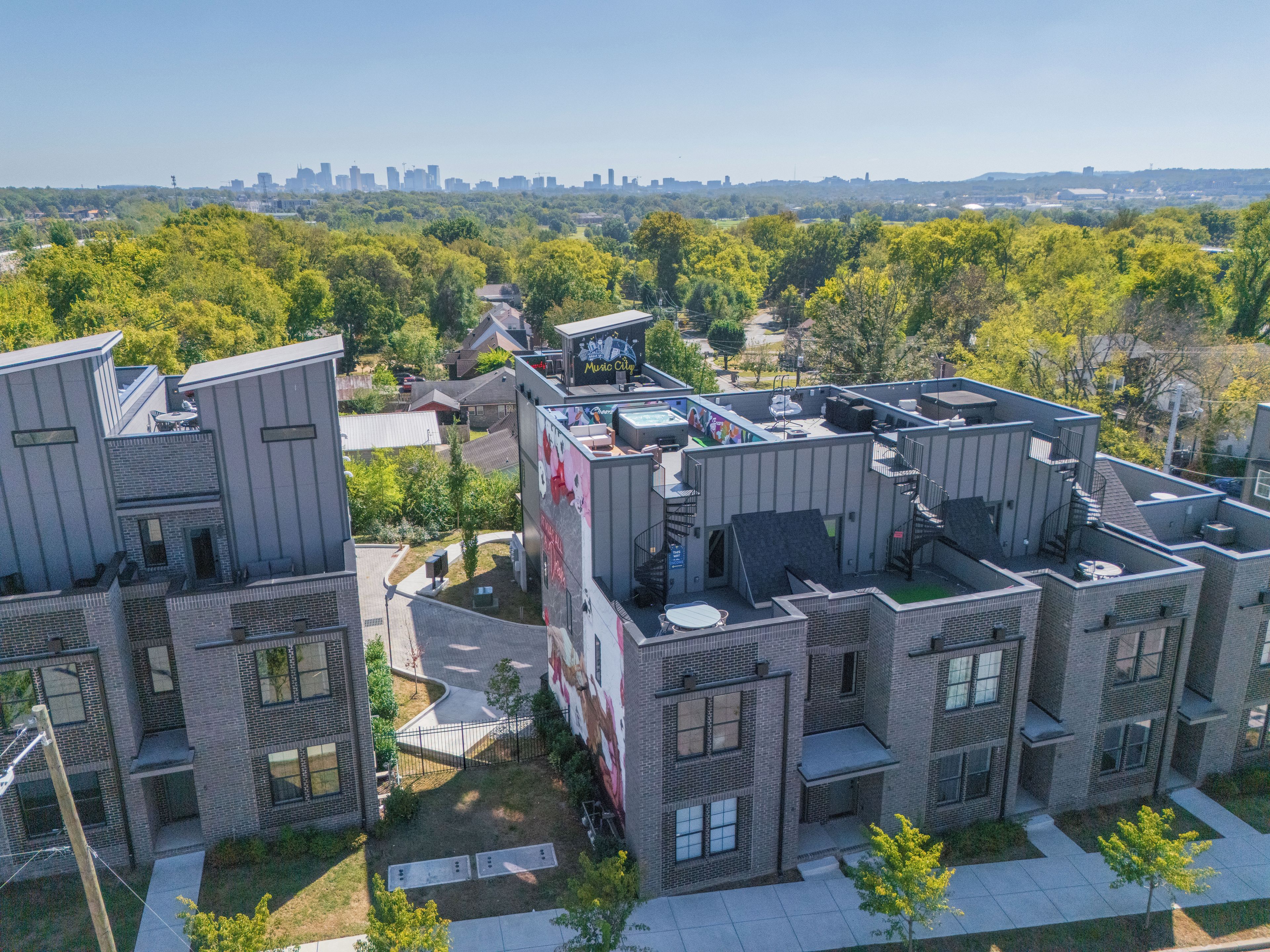 A modern apartment complex with multiple buildings, a rooftop pool, and a city skyline in the background.